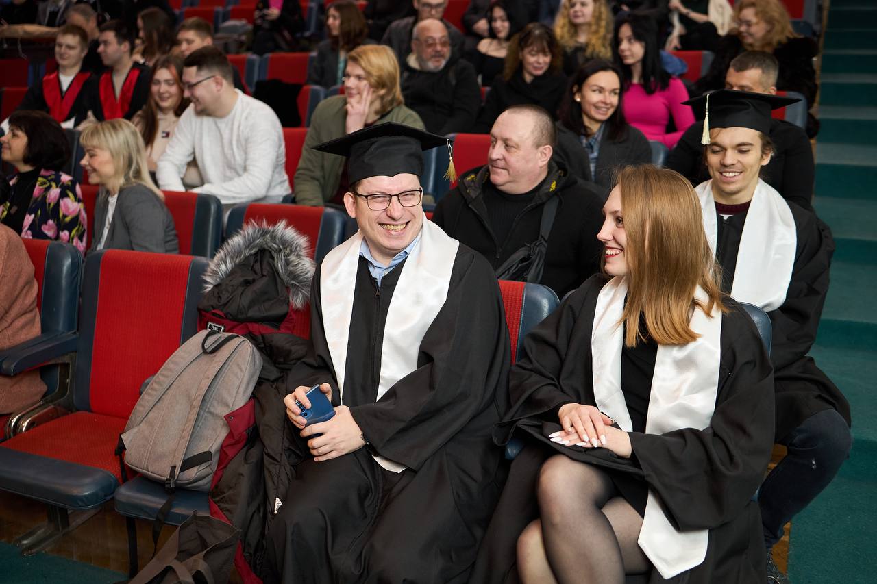 Студенти в одязі для випускного сидять на червоних кріслах 