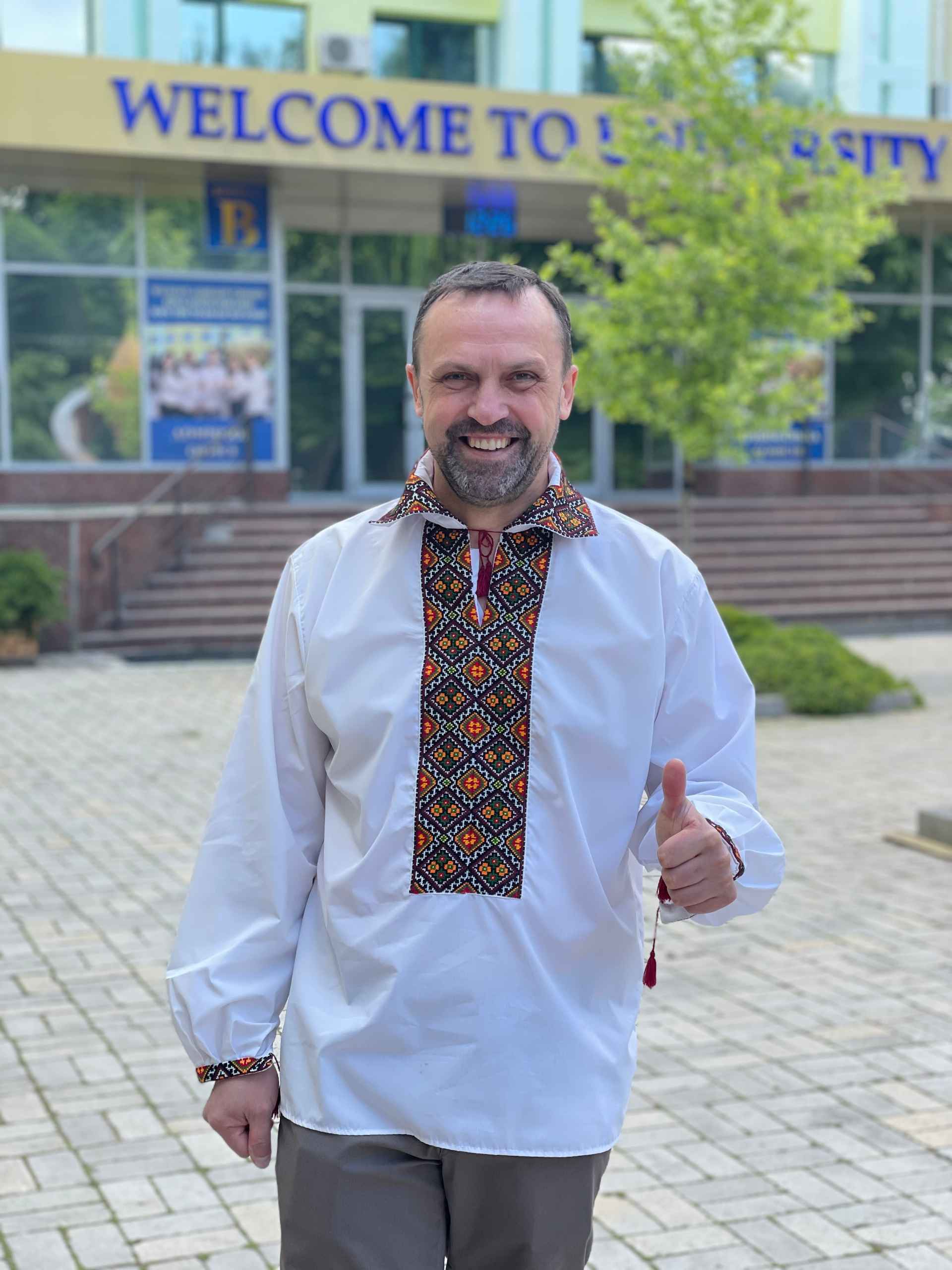 Чоловік, що стоїть перед Університетом імені Альфреда Нобеля у традиційному українському одязі, показує великий палець угору 
